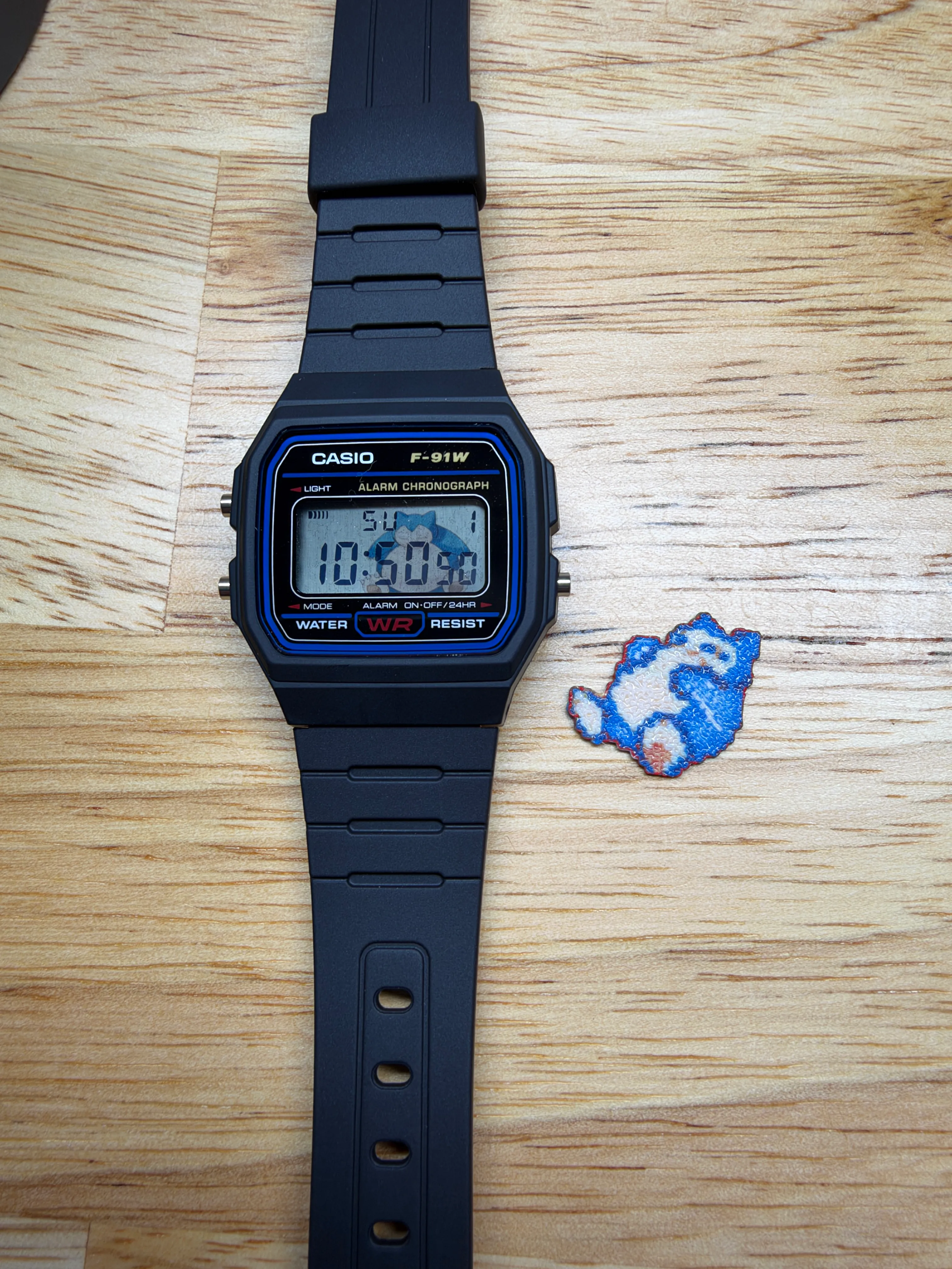 Front view of the Snorlax F-91W on a wood surface, with a small Snorlax artwork piece beside it