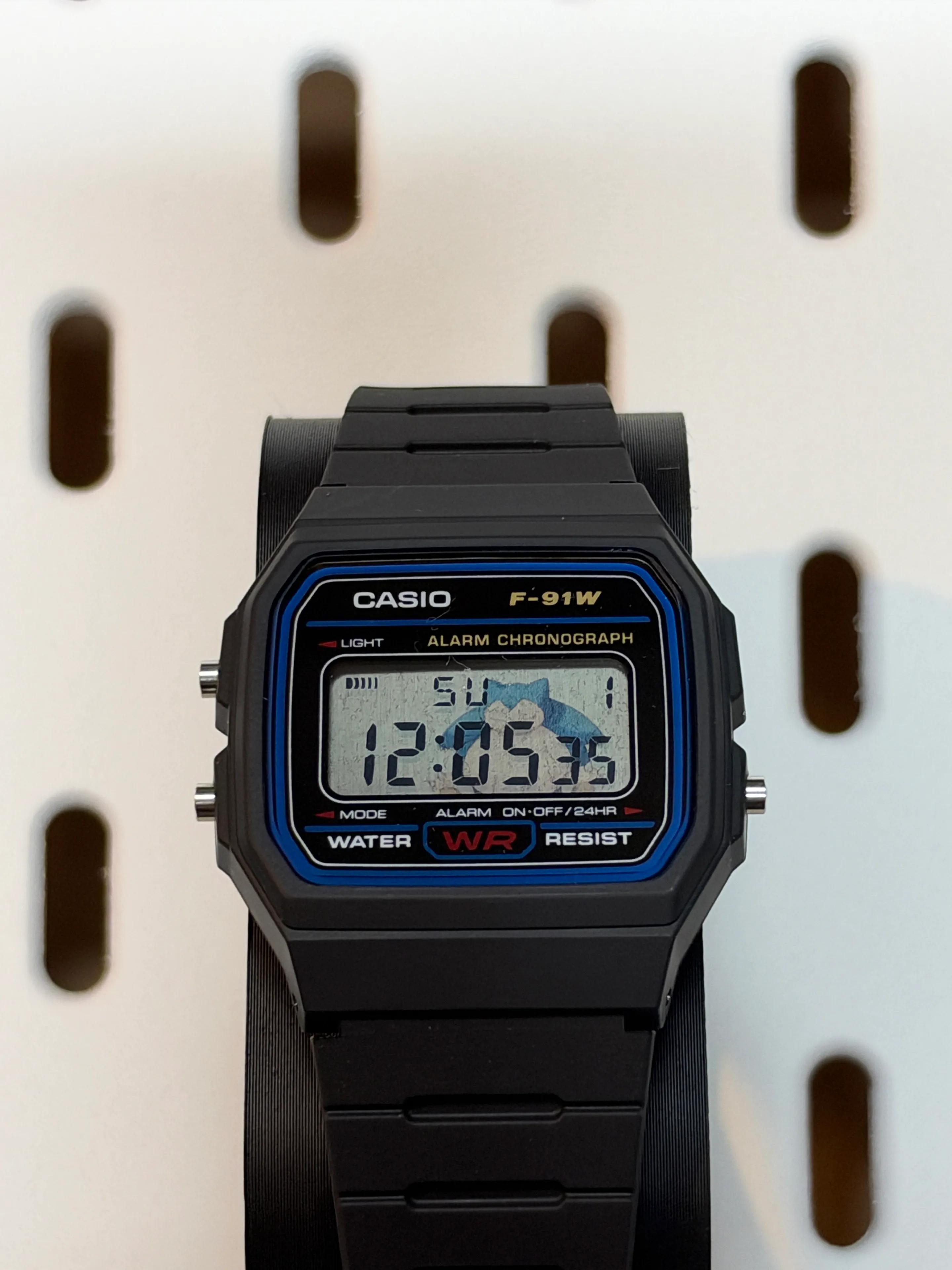 Front view of the black Casio F-91W with Snorlax artwork visible behind the LCD